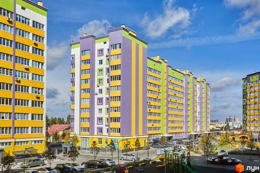 Яскраві багатоповерхові будинки ЖК Щасливий на Яблуневій з різнокольоровими фасадами. Поруч дитячий майданчик та місця для паркування.