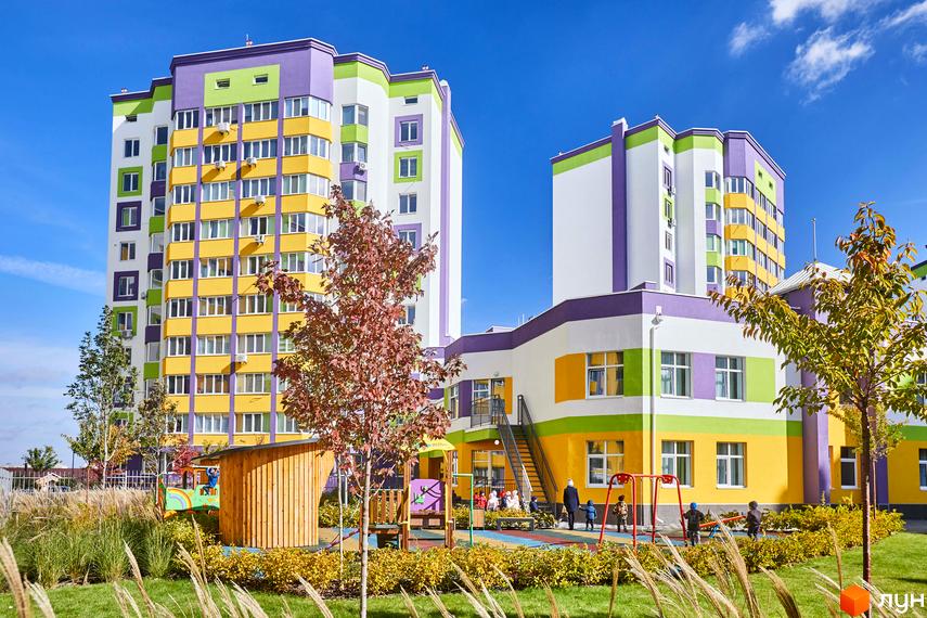 Житловий комплекс Щасливий на Яблуневій: яскрава фасадна частина будівель з різнокольоровими елементами (жовтий, зелений, фіолетовий) та дитячий майданчик з гойдалками та пісочницею.