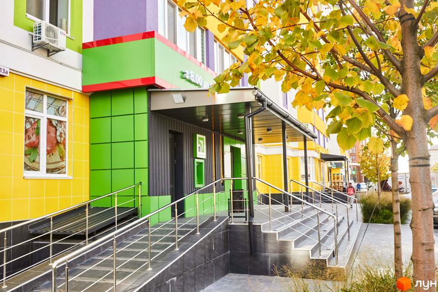 Житловий комплекс Щасливий на Яблуневій. Фасад будинку оздоблений яскравими кольорами: жовтим, зеленим та фіолетовим. Біля входу розташовані сходи з поручнями та навісом.