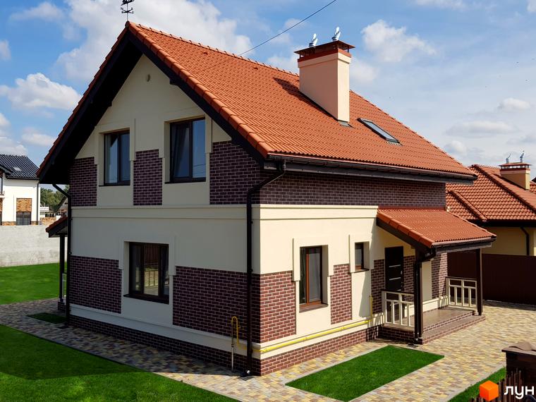 Котеджне містечко Сонячний: двоповерховий будинок з червоною черепичною покрівлею, цегляним та світлим фасадом, зеленим газоном та бруківкою перед будинком.