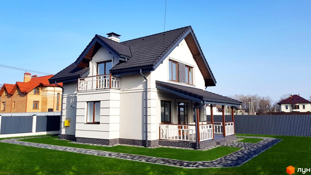 Котеджне містечко КМ Сонячний: двоповерховий будинок з темним дахом, білими стінами, балконом та навісом над входом. Прибудинкова територія з доглянутим газоном та доріжками.