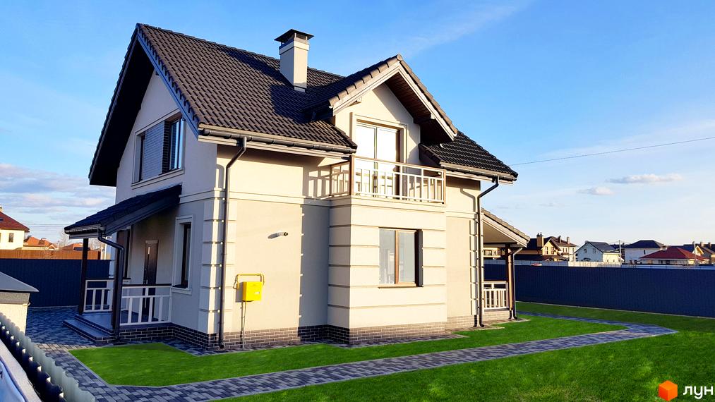 Котеджне містечко КМ Сонячний: двоповерховий будинок світло-бежевого кольору з темним дахом, балконом та доглянутою прибудинковою територією з газоном та доріжками.