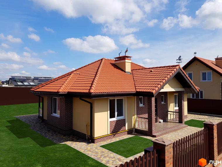 Котеджне містечко Сонячний: одноповерховий будинок з червоною черепичною кришею, цегляним та світлим фасадом, розташований на зеленій ділянці з доріжками та парканом.