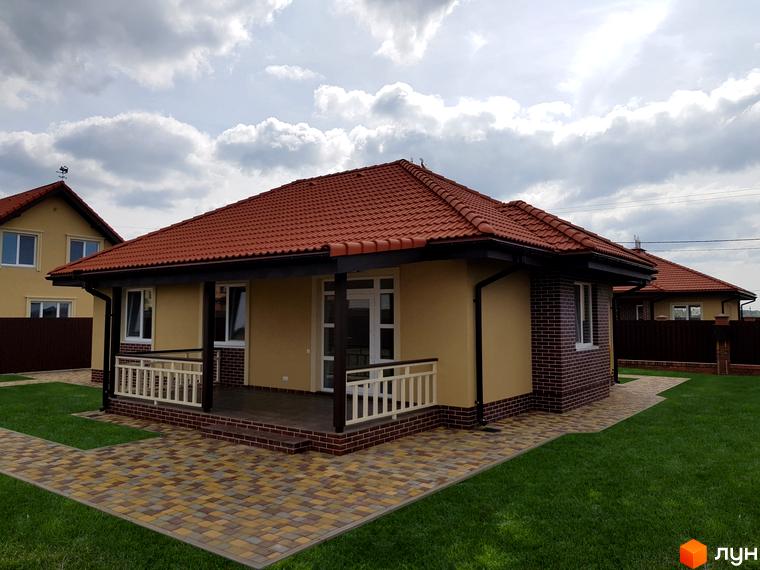 Котеджне містечко Сонячний: одноповерховий будинок з червоною черепичною кришею та жовтими стінами. Прибудинкова територія з акуратним газоном та бруківкою.