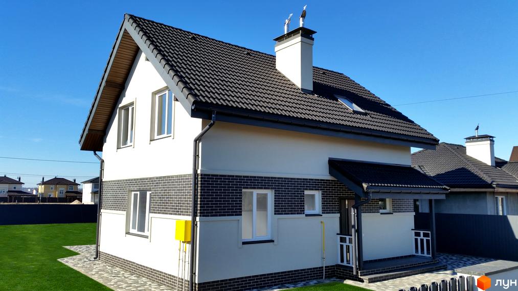 Котеджне містечко КМ Сонячний: двоповерховий будинок з темним дахом, білими стінами та цегляним оздобленням фасаду, зелений газон та бруківка біля будинку.