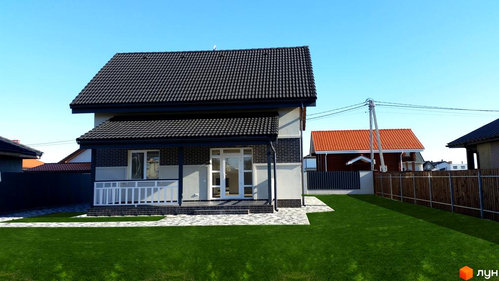 Котеджне містечко Сонячний: двоповерховий будинок з темним дахом, білою огорожею та зеленим газоном. Навколо будинку розташована бруківка та паркан.