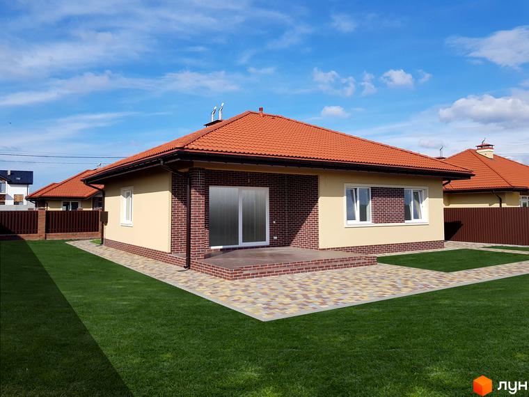 Котеджне містечко КМ Сонячний: одноповерховий будинок з червоним черепичним дахом, світлими стінами та цегляним оздобленням. Прибудинкова територія з доглянутим газоном та бруківкою.