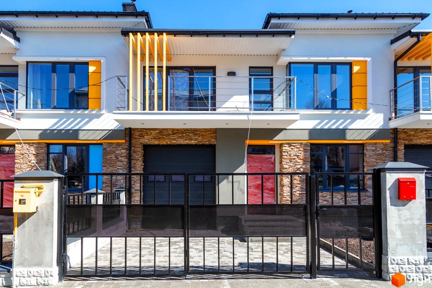 Фасад новобудови на вул. Насінна, 7 з великими вікнами та кам'яним оздобленням. Огороджена прибудинкова територія з воротами та поштовими скриньками.