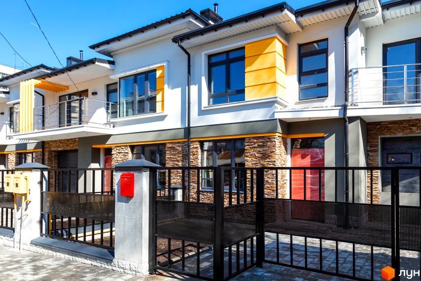 Зовнішній вигляд новобудови на вулиці Насінній, 7, з фасадом білого кольору та жовтими акцентами. Прибудинкова територія огороджена чорною металевою огорожею.