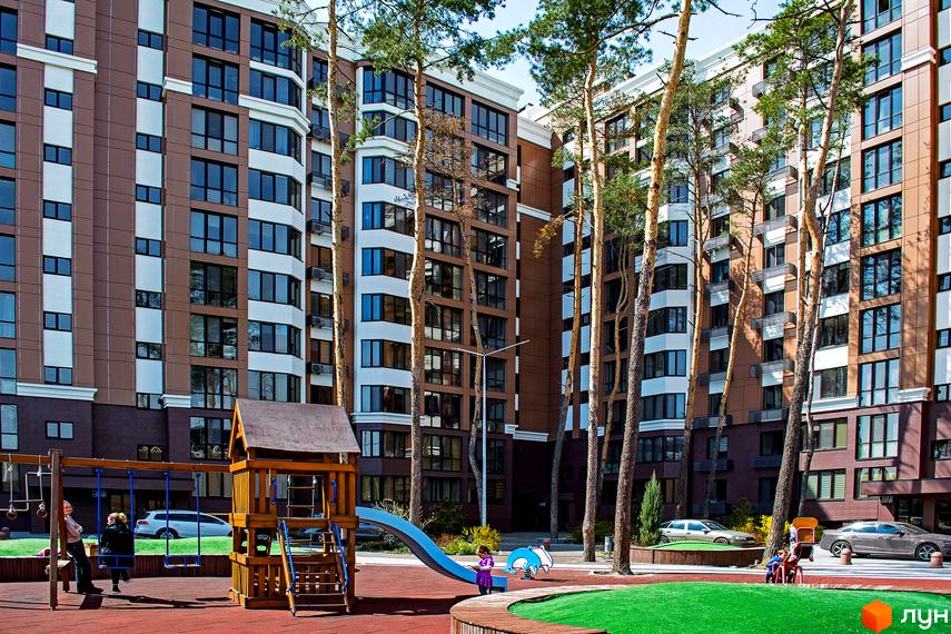 Житловий комплекс Echo Park з коричнево-білими фасадами та великою кількістю вікон. На прибудинковій території розташований дитячий майданчик з гіркою та гойдалками.