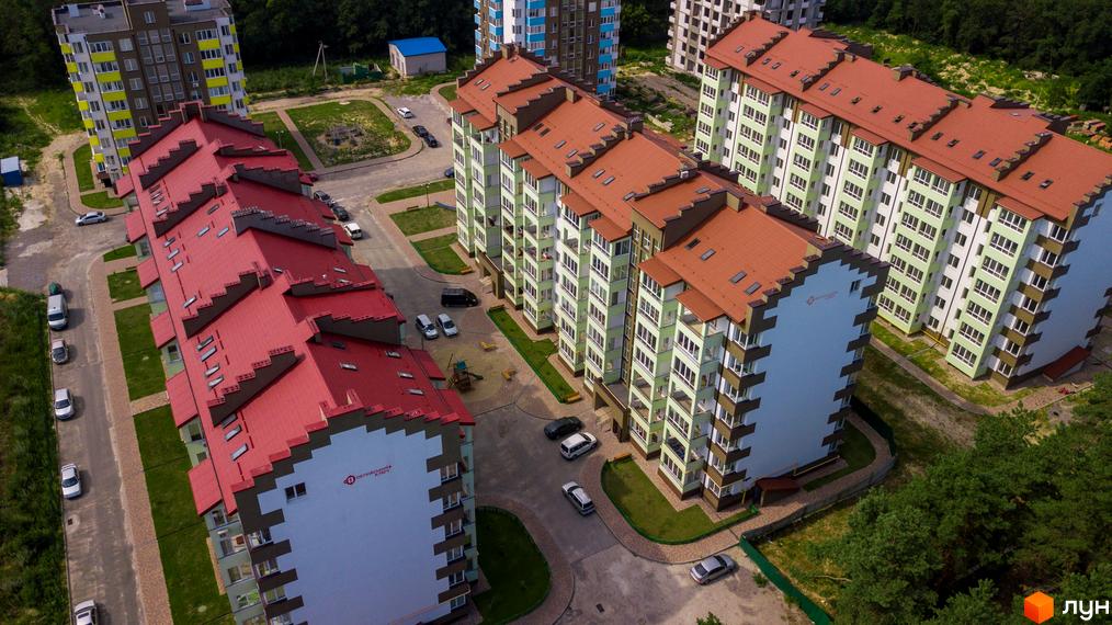 Житловий комплекс Обухівський ключ. Багатоквартирні будинки з червоними дахами та світлими фасадами. На прибудинковій території є парковка та дитячий майданчик.