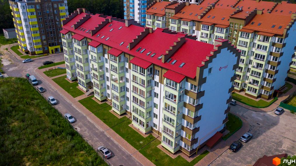 Житловий комплекс Обухівський ключ з червоним дахом на тлі зеленої території. Багатоквартирний будинок з балконами та вікнами, розташований серед інших будівель.
