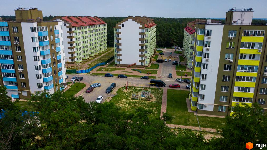 Житловий комплекс Обухівський ключ. Високі будинки з різнокольоровими фасадами та червоними дахами. На території комплексу є парковка для автомобілів та дитячий майданчик.