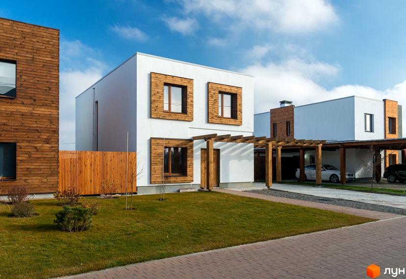 Котеджне містечко На Щасливій: двоповерхові будинки з дерев'яними елементами та навісами для авто. Зелена галявина та доріжка з бруківки перед будинками.