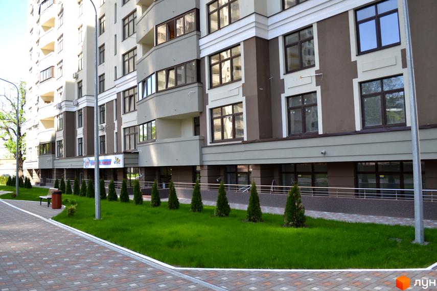 Зовнішній вигляд новобудови Зелений острів-2 з акуратним газоном та висадженими туями. На території є лавка та урни для сміття.