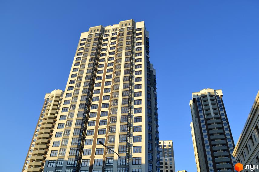 Зовнішній вигляд висотних будинків житлового комплексу Зелений острів-2 на фоні блакитного неба. Будинки мають багато вікон та балконів.