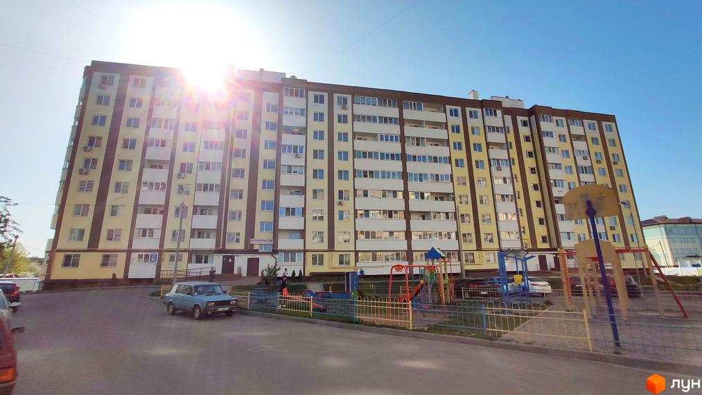 Багатоповерховий будинок ЖК Банківський з жовтим фасадом та балконами. На прибудинковій території дитячий майданчик та парковка.