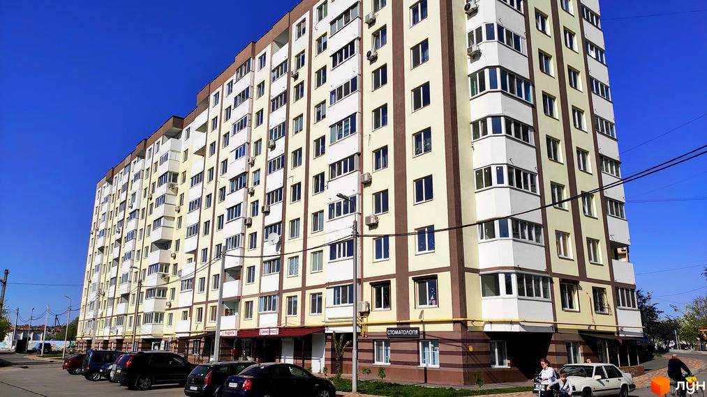 Житловий комплекс Банківський: багатоповерховий будинок бежево-коричневих кольорів з балконами та вікнами. Перед будинком розташована парковка з автомобілями.