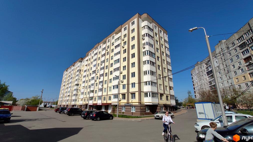 Житловий комплекс Банківський: багатоповерховий будинок світло-жовтого кольору з коричневими акцентами. Навколо парковка, дерева та вулиця.