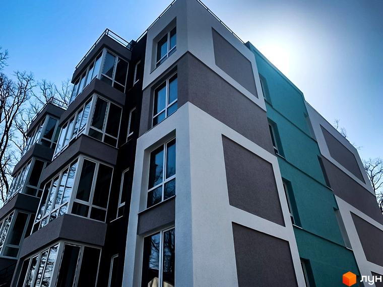 Фасад Житлового комплексу ColibriHouse з сірими, білими та бірюзовими секціями, великими вікнами. Навколо будинку видно безлисті дерева.