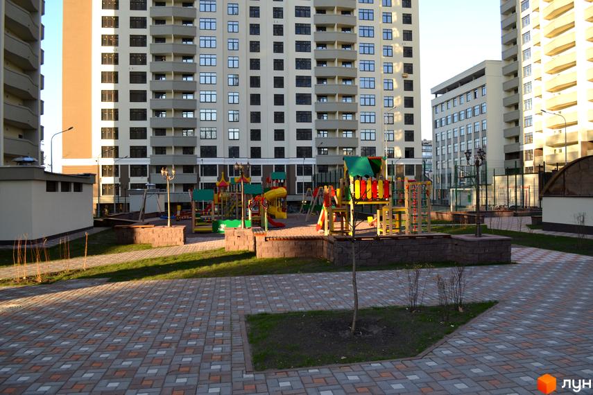 Зелений острів-2: Багатоповерхові житлові будинки з численними вікнами. Прибудинкова територія включає дитячий майданчик та доріжки.