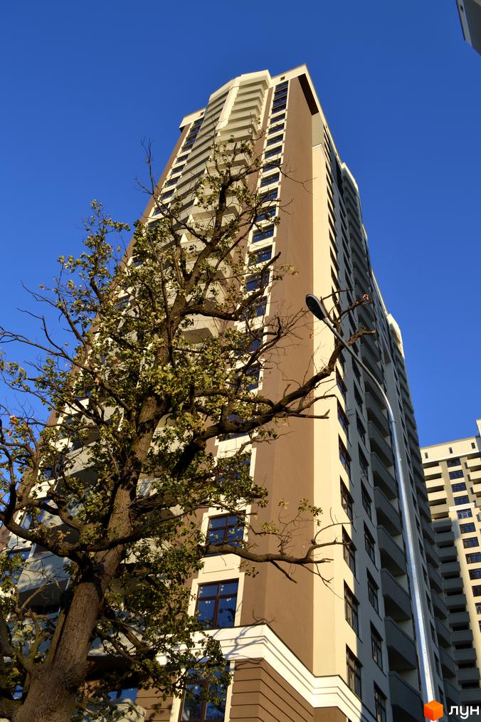 Зовнішній вигляд будинку Зелений острів-2 з фасадом кольору слонової кістки та коричневого кольору. Поруч високе дерево з зеленою кроною.