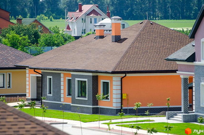 Будинок житлового комплексу КМ Green Town з червоною покрівлею та оранжевими стінами. Прибудинкова територія з зеленими насадженнями та доріжками.