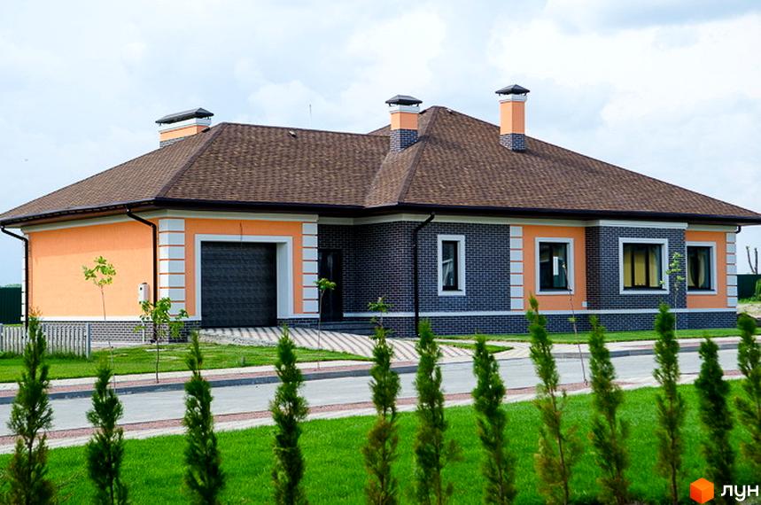Котеджне містечко КМ Green Town. Одноповерховий будинок з помаранчевою та сірою цегляною обробкою, коричневим дахом та двома димарями. Прибудинкова територія з доглянутим газоном та зеленими насадженнями.