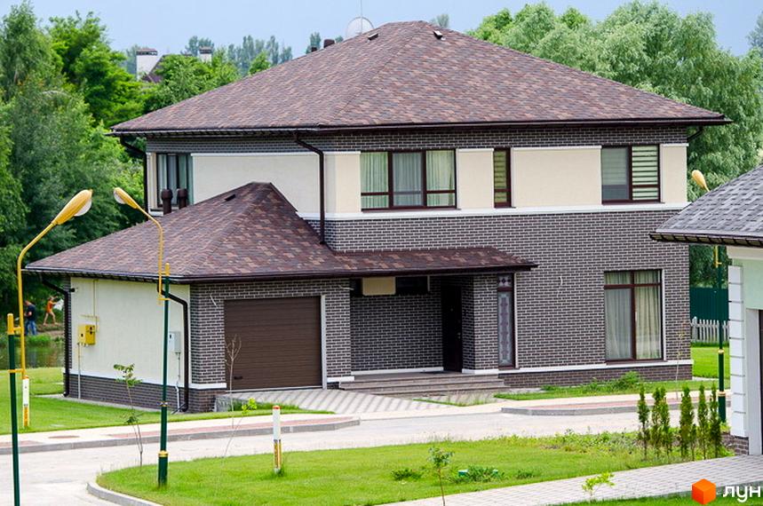Котеджне містечко КМ Green Town. Зовнішній вигляд двоповерхового будинку з цегляним фасадом, гаражем та прибудинковою територією з газоном та ліхтарями.