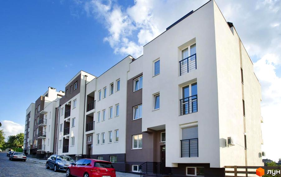 Житловий комплекс Панорама – біло-сіра багатоповерхівка з балконами. Вулиця перед будинком вимощена бруківкою, припарковані автомобілі.