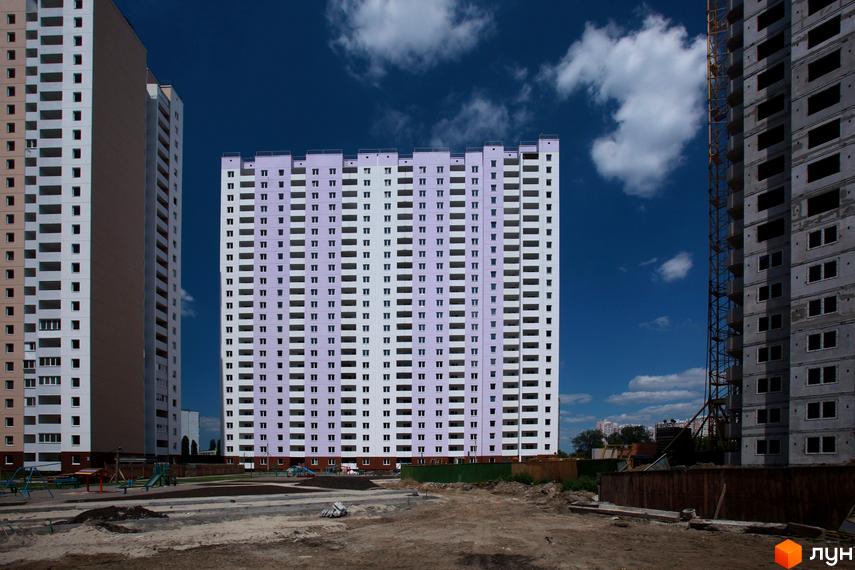 Житловий комплекс на вулиці Урлівській, 38а. Багатоповерхові будинки з численними вікнами та балконами на тлі блакитного неба з хмарами. На передньому плані будівельний майданчик з елементами дитячого майданчика.