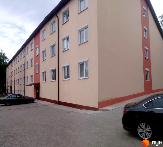 Будинок на Петровського - новобудова з світло-бежевим фасадом та червоними вставками. Прибудинкова територія з бруківкою та припаркованими автомобілями.