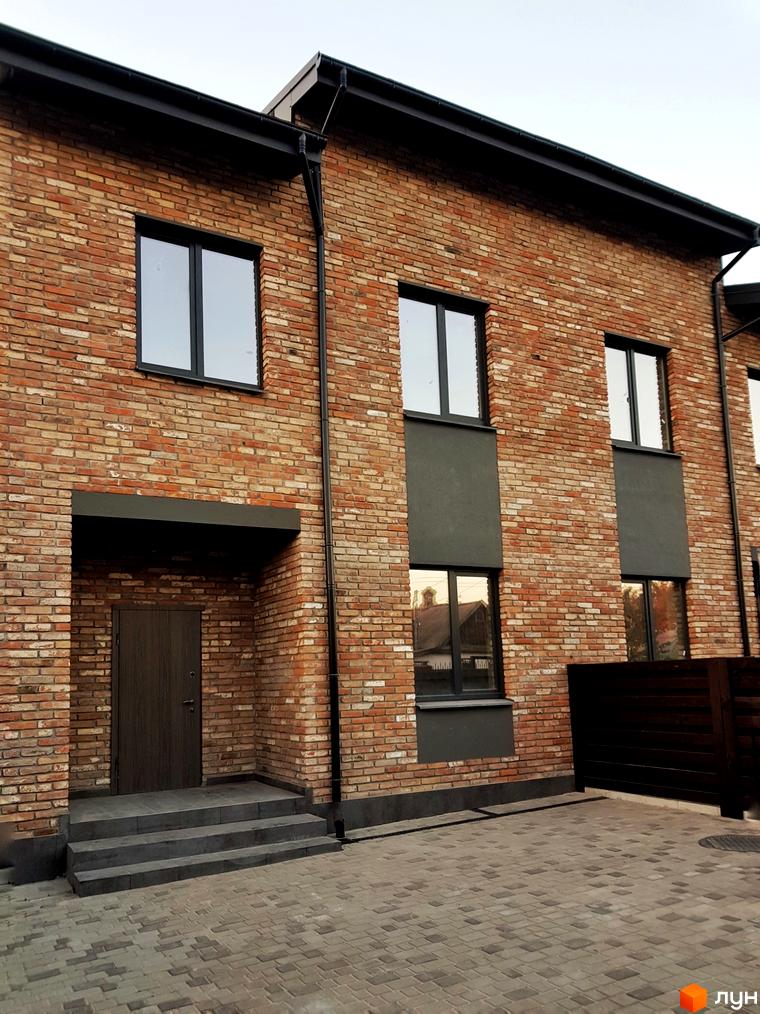 Таунхауси Пушкінський: двоповерховий будинок з червоної цегли, сірими вікнами та дверима, вимощення з бруківки та дерев'яний паркан. Зовнішній вигляд новобудови.