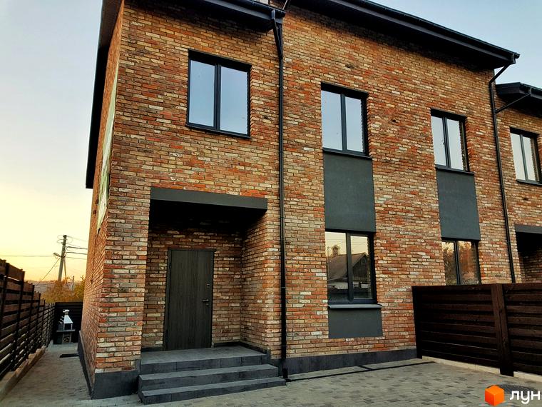 Таунхауси Пушкінський: двоповерховий будинок з цегляним фасадом та темними вікнами. Поруч розташована брукована доріжка та дерев'яний паркан.