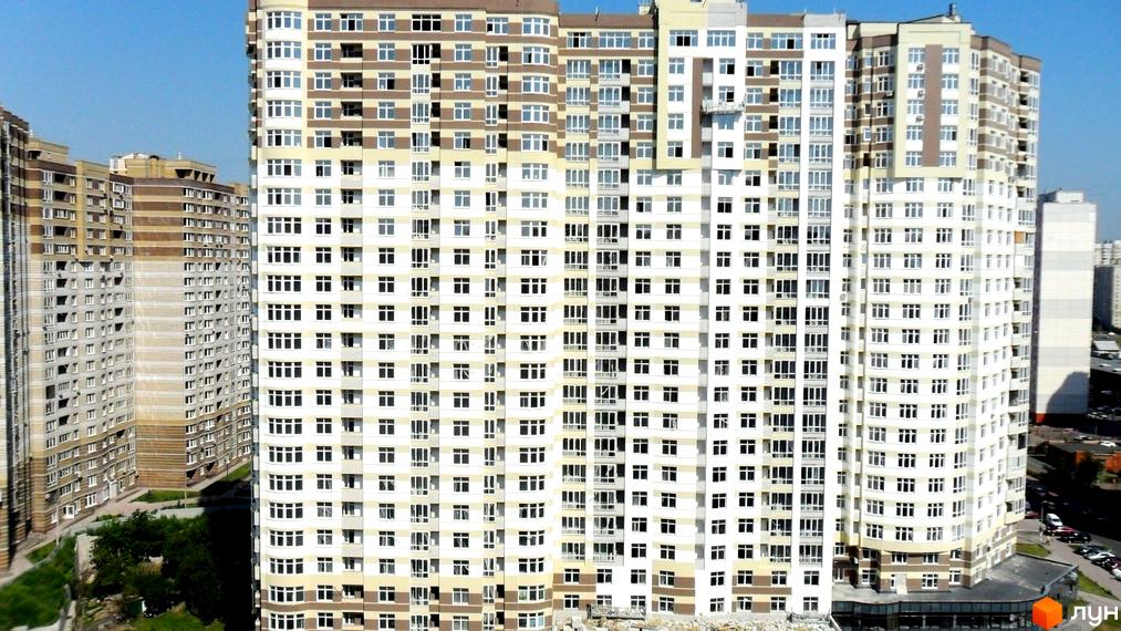 Новобудова житлового комплексу на вул. Ахматової, 22, Позняки-2, з біло-бежевим фасадом, численними вікнами та прилеглою зеленою зоною.