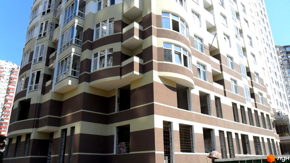 Новобудова на Ахматової 22, Позняки-2, з коричнево-бежевим смугастим фасадом та округлими кутами. Видно багато вікон та елементи будівництва.