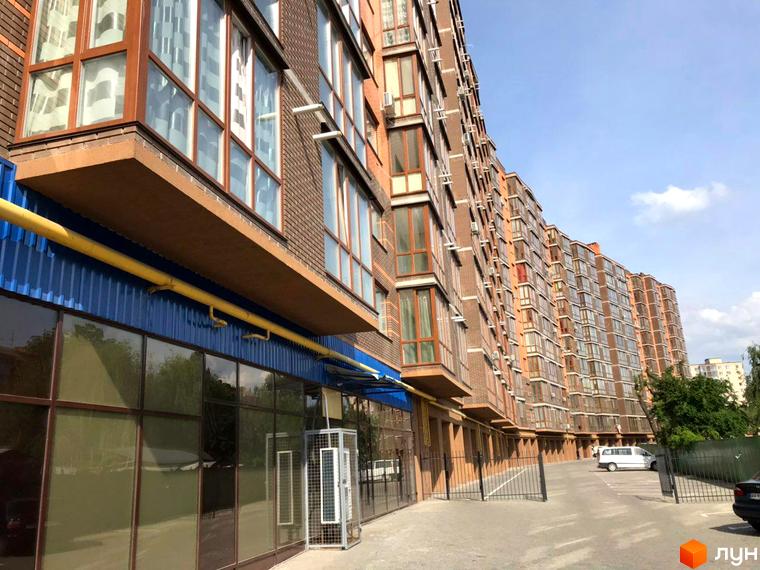 Зображення фасаду Житлового комплексу Сімейний. Багатоповерховий будинок з великими вікнами та балконами, перед будинком облаштована парковка.