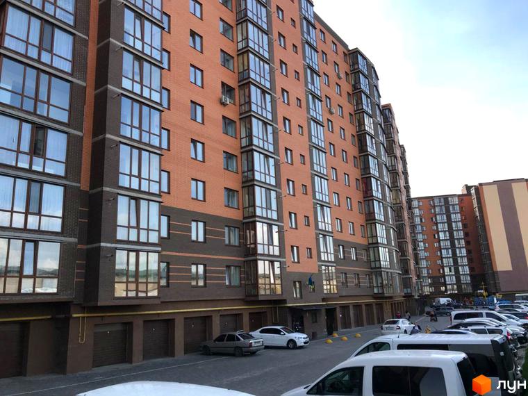 Зображення фасаду Житлового комплексу Сімейний, цегляний будинок з великими вікнами. На передньому плані припарковані автомобілі.