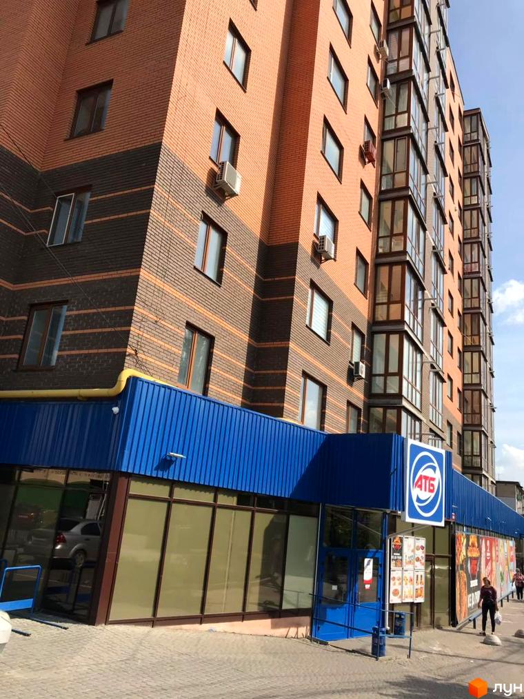 Зображення фасаду багатоповерхового будинку в Житловому комплексі Сімейний. Вигляд на будівлю з магазином на першому поверсі.