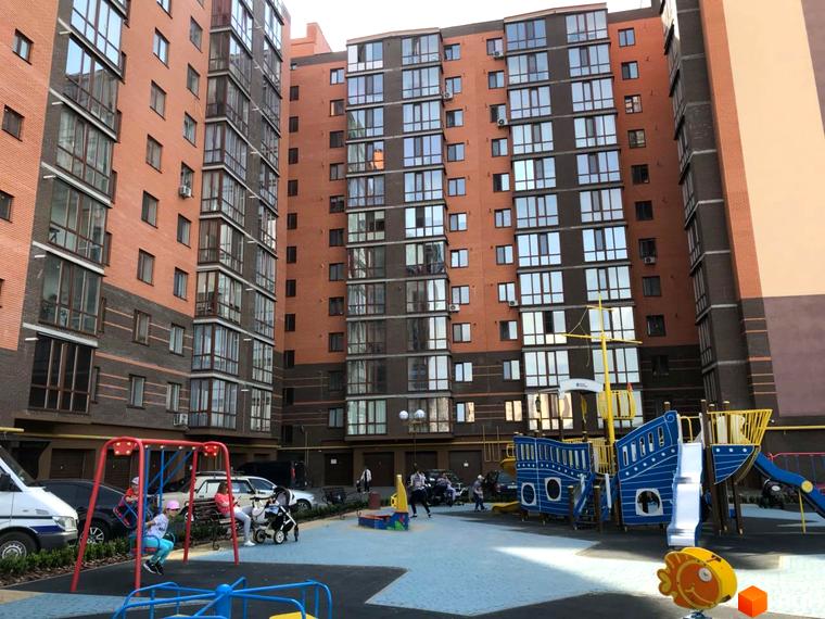 Зображення Житлового комплексу Сімейний. Вигляд багатоповерхового будинку з червоної цегли та дитячий майданчик у дворі.