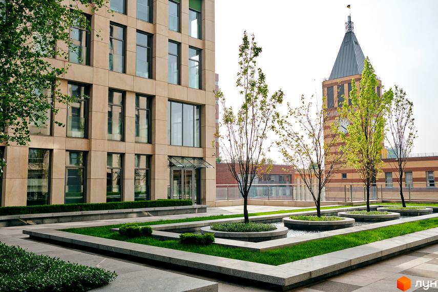 Сучасна будівля ЖК Cascade Plaza з великими вікнами та прибудинковою територією, озелененою газонами та деревами.