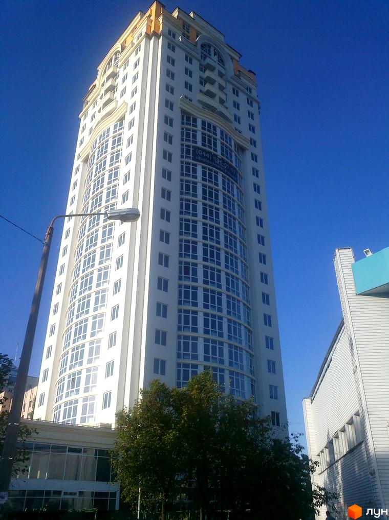 Зображення висотної будівлі ЖК Obolon Tower з великою кількістю вікон. Вид на фасад будинку та частину прилеглої території.