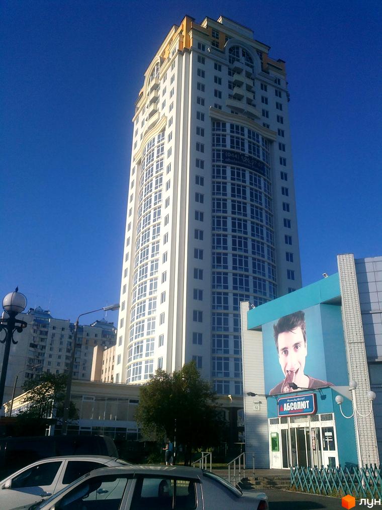 Зображення фасаду Новобудови Оболонь Тауер. Висотна будівля з великою кількістю вікон на фоні блакитного неба.