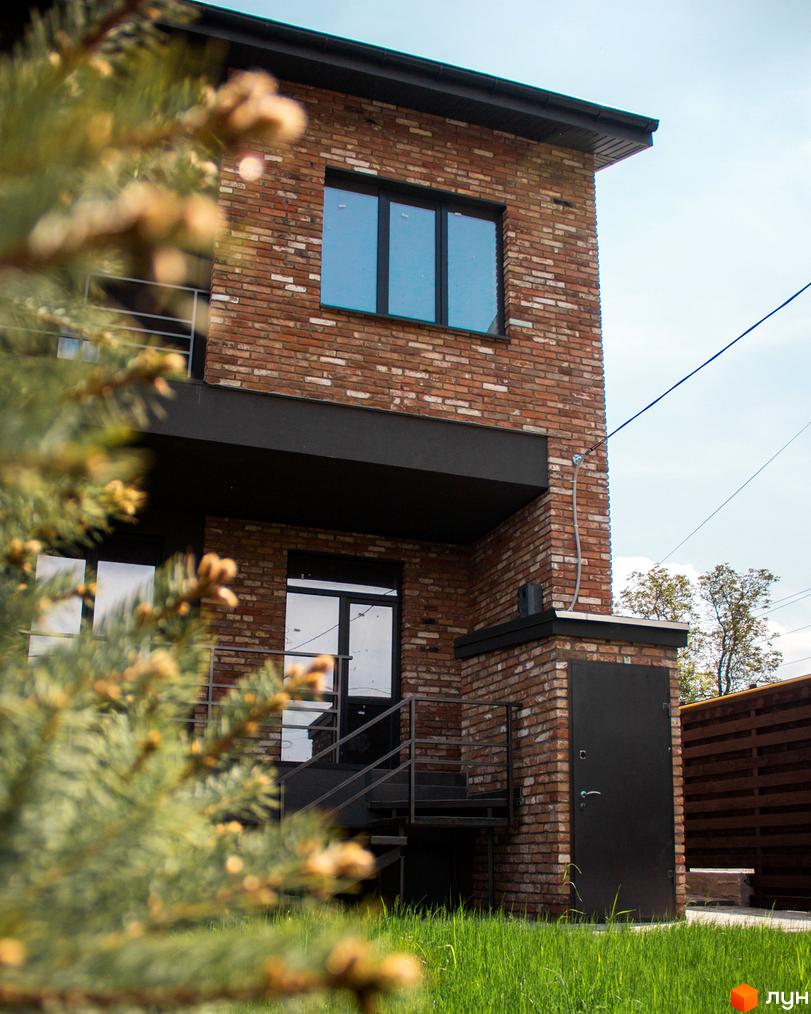 Таунхауси Пушкінський: двоповерховий будинок з цегляним фасадом та чорними вікнами. Поруч зелена галявина та дерев'яний паркан.