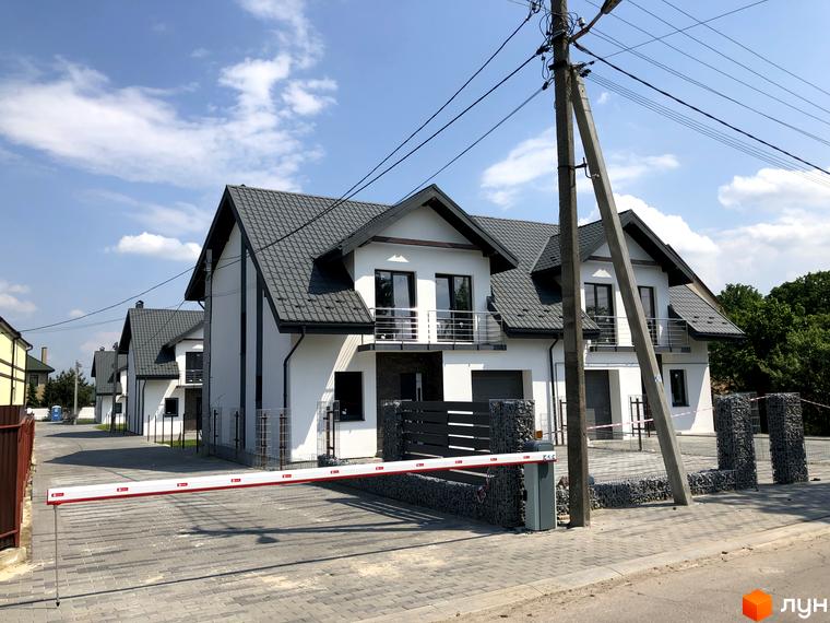 Вигляд котеджів у Котеджному містечку Європа з сірими дахами та білими стінами. На передньому плані автоматичний шлагбаум та дорога з тротуарної плитки.