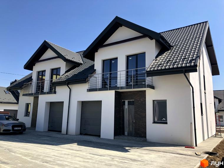 Котеджне містечко КМ Європа: фасади білих будинків з темними дахами та гаражними воротами, прибудинкова територія з бруківкою та автомобілем.