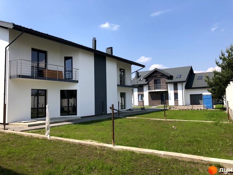 Котеджне містечко КМ Європа: фасади білих будинків з темними дахами та балконами, прибудинкова територія з газоном та огорожею.