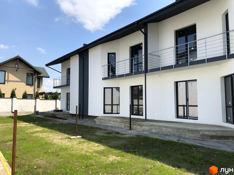 Зображення фасаду та балконів двоповерхового будинку в Котеджному містечку Європа. На передньому плані зелений газон.