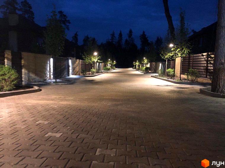 Котеджне містечко Zahrava Village. Нічна дорога з бруківки освітлена ліхтарями, що веде до будинків з парканами та деревами.