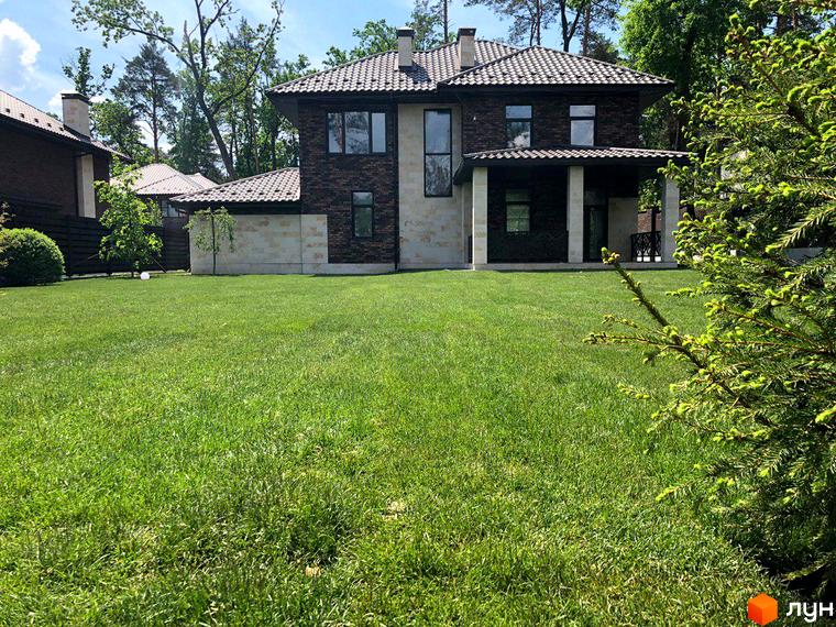 Котеджне містечко КМ Zahrava Village. Зовнішній вигляд двоповерхового будинку з цегляним фасадом та великою зеленою галявиною перед ним.